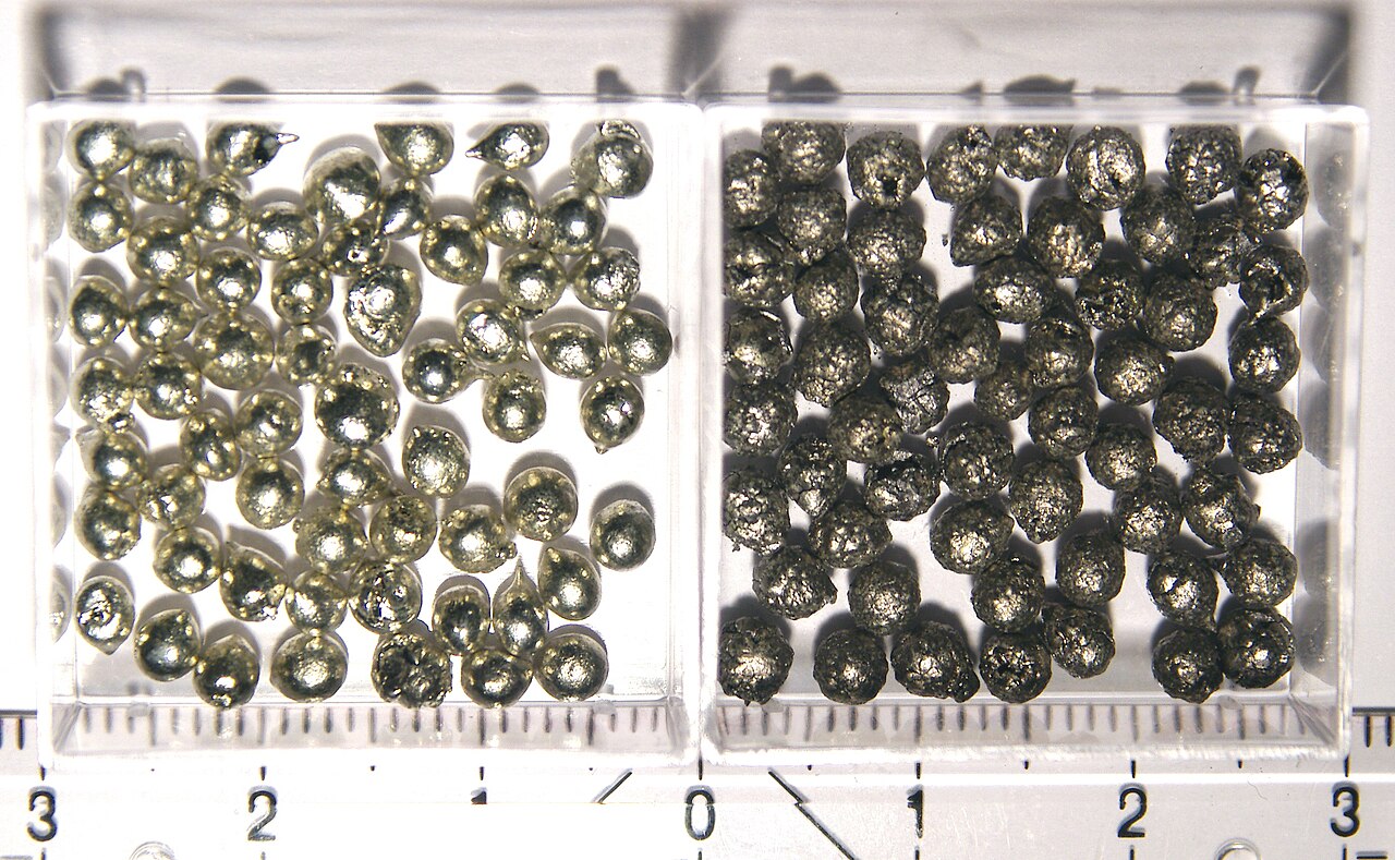 Two clear trays of tin beads over a ruler: shiny silver beads on the left, dull, crusty dark grey ones on the right.